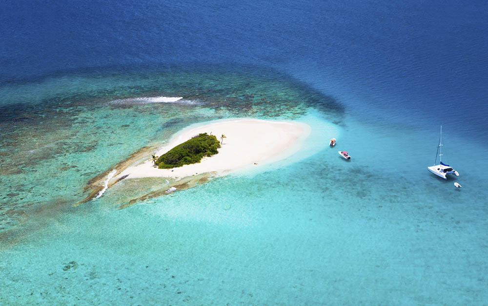 aerial shot of a deserted island in British Virgin Islands with boats anchored by