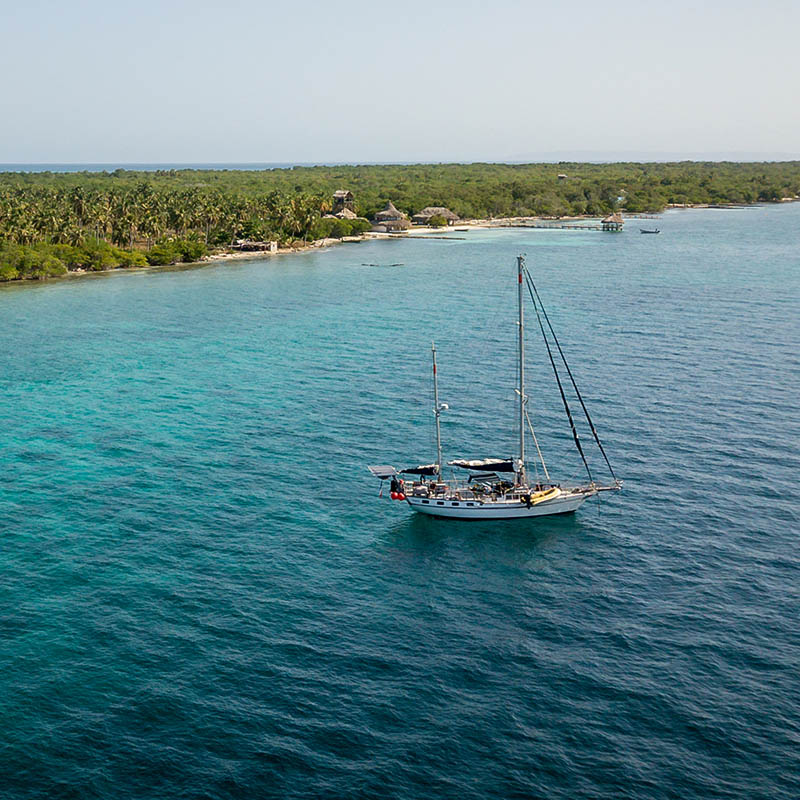 A sailing boat anchored in blue water sea with the island Islas de San Bernardo, Colombia