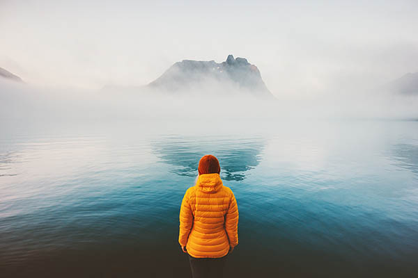 Woman standing looking at island covered in mist, Scandinavia