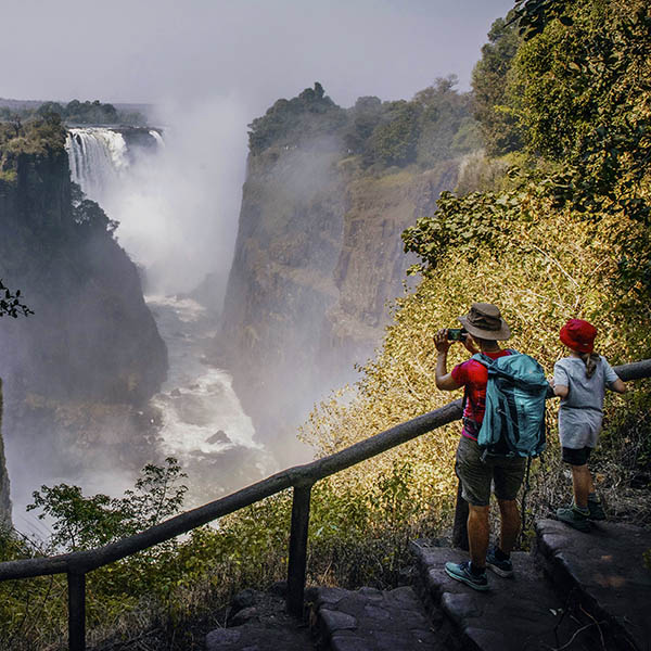 Tourist with child photographing Victoria Falls in the late afternoon with rainbow, Zambezi, Zimbabwe