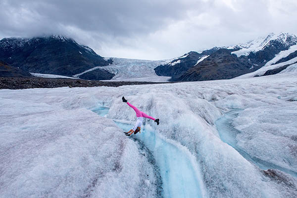 A woman doing yoga on a glacier surrounded by mountains in Alaska