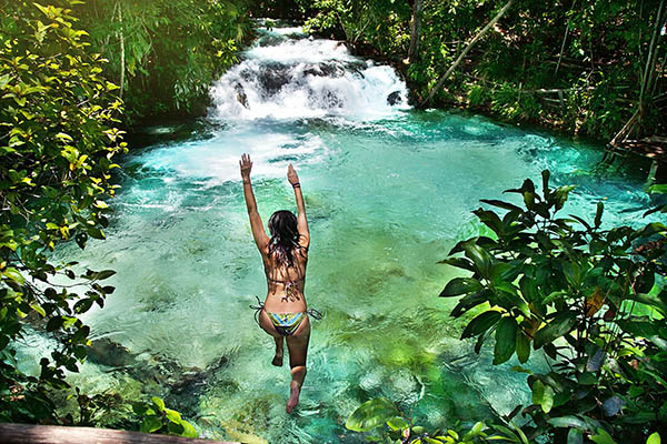 Woman jumping into a waterfall, in a forest in Brazil