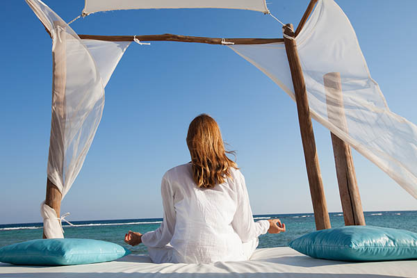 Woman in yoga pose sitting at the seashore under a shade