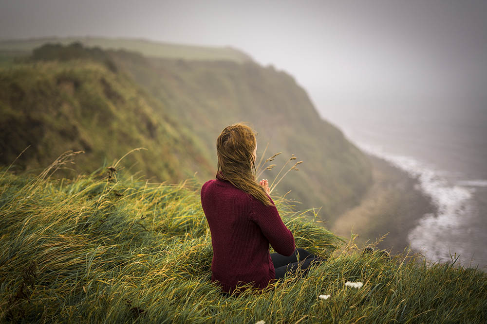 Woman sitting on cliff edge in the misty morning