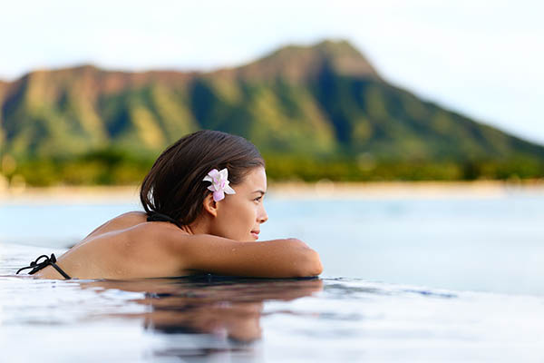 Infinity pool resort woman relaxing at sunset overlooking Waikiki beach in Honolulu city, Oahu island, Hawaii, USA.