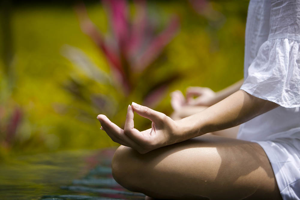 Woman sitting in tropical setting in yoga pose