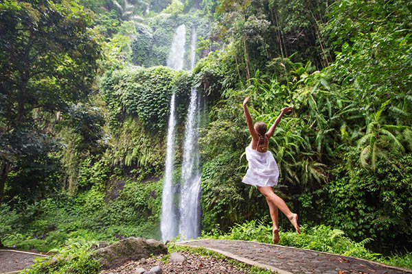 Woman meditating doing yoga between waterfalls near Rinjani, Senaru, Lombok, Indonesia