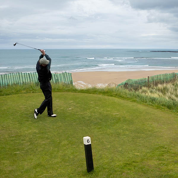 Man swinging club while golfing by the ocean in County Clare, Ireland