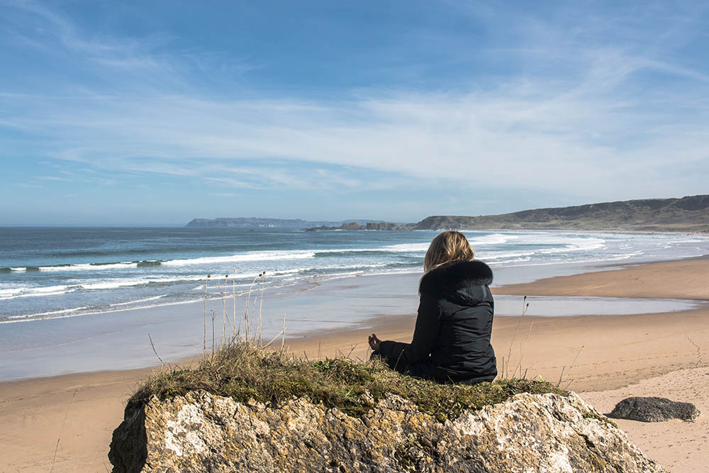 Girl sitting in yoga position on a beach in Ireland