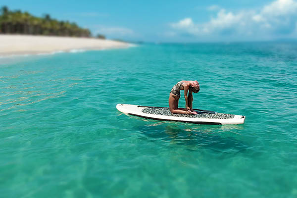 Girl in in yoga pose on SUP paddleboard of a tropical island