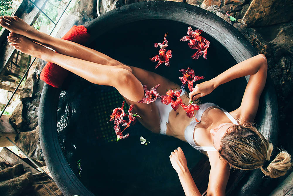 Woman relaxing in round outdoor bath with tropical flowers. Organic skin care in kawa hot bath in luxury spa resort