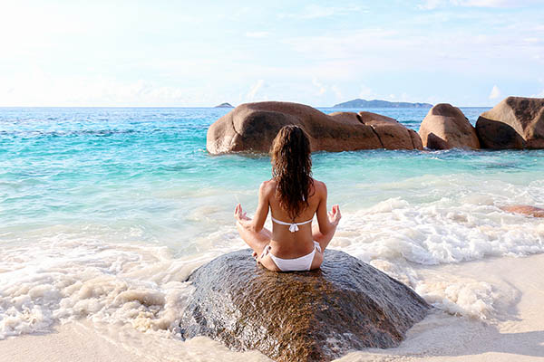 Young woman in yoga pose on a rock by the sea on Praslin Island, Seychelles