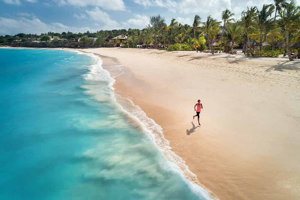 Aerial view of woman running on white sandy beach on Zanzibar