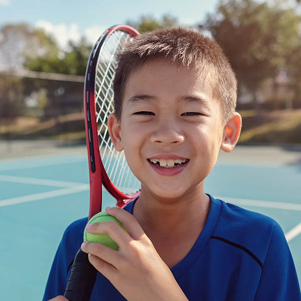 Happy young Asian boy tennis player on outdoor blue court