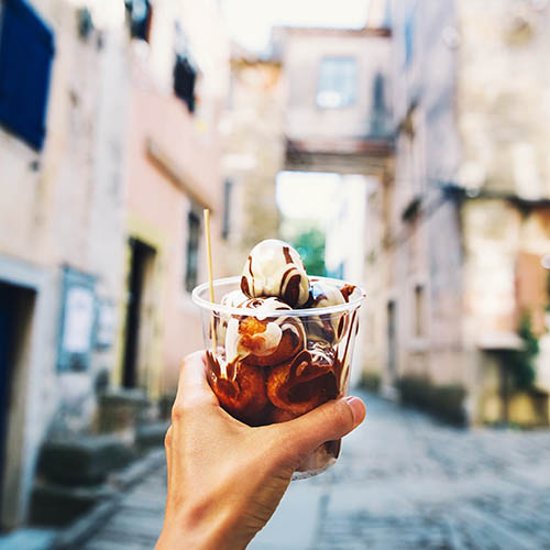 Close up of a hand holding Fritule, traditional Croatian sweet pastry, against background of streets in Croatia