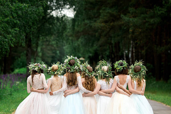 back view of a bride in a white dress standing and embracing bridesmaids