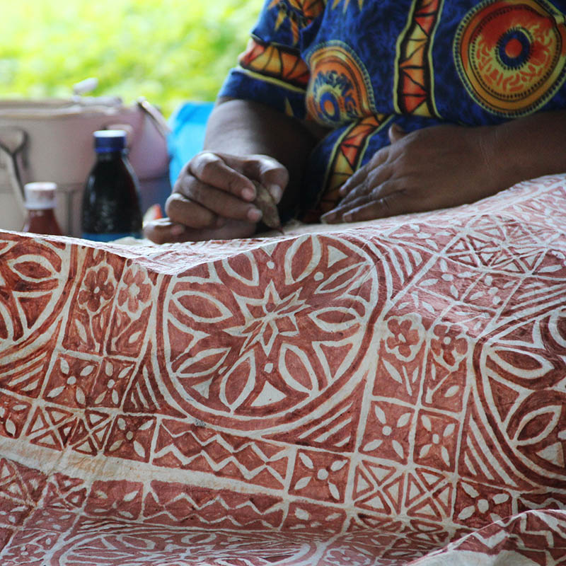 A Samoan lady drawing traditional pattern with mud water on a handmade mulberry paper