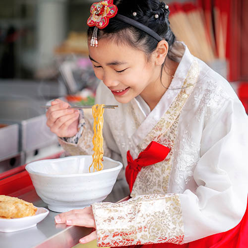 Korean girl in traditional dress eating noodles in a restaurant in Seoul City, South Korea