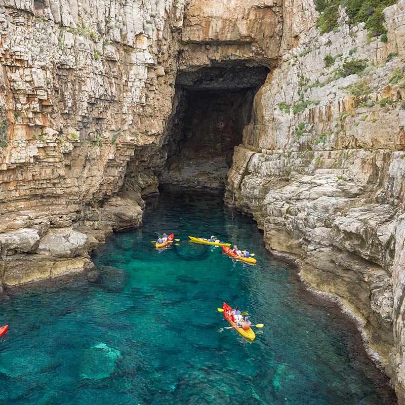 View from the rock cliffs of kayakers exploring the crystal clear Mediterranean waters of a cove off the coast of Dubrovnik, Croatia