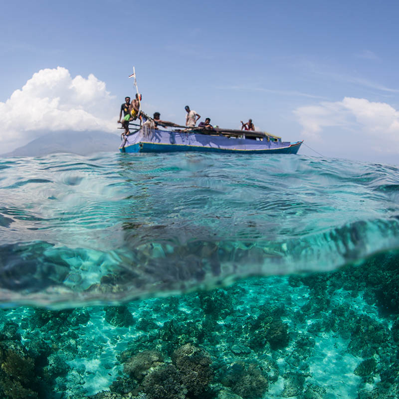 Indonesian fishermen, from the island of Flores, sit on their boat near a coral reef