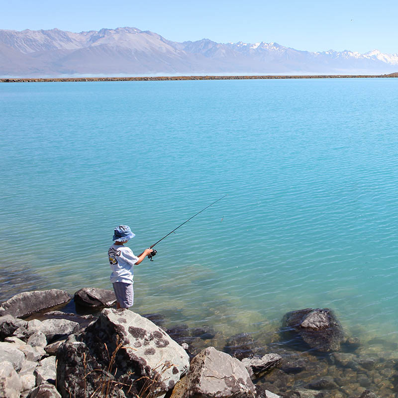 Young boy fishing from the shore of a lake in New Zealand