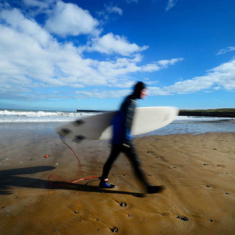 Surfer striding across Aberdeen Beach with Surf Board, Scotland