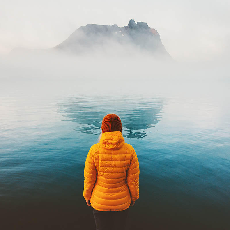 Woman standing looking at island covered in mist, Scandinavia