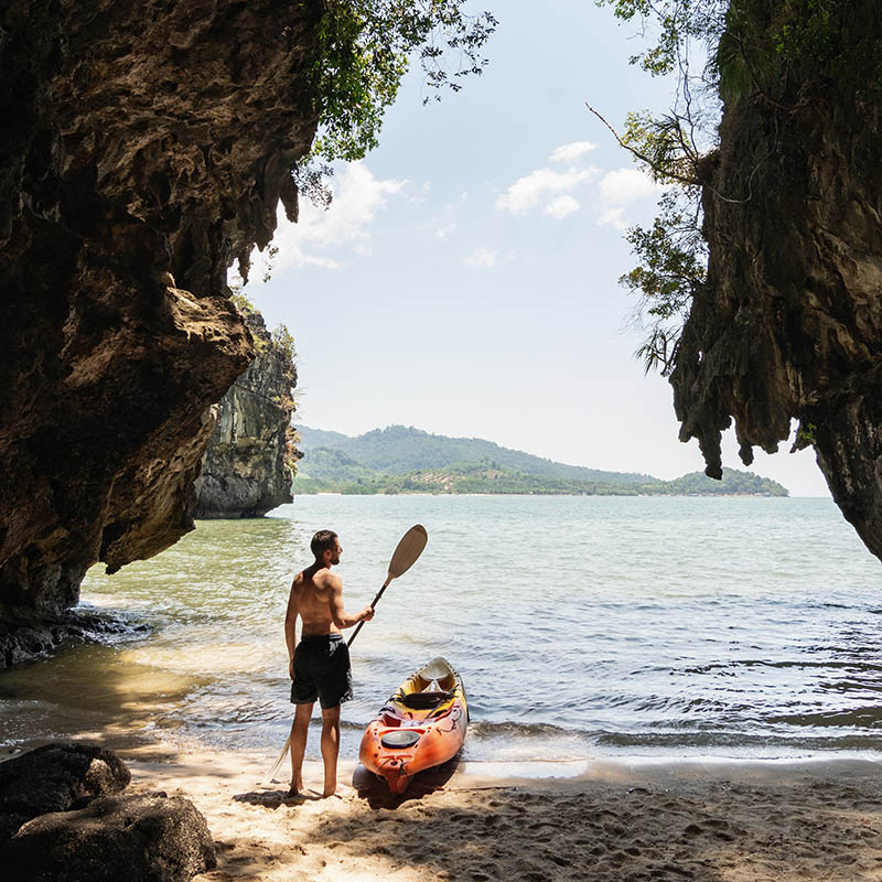 Man with a paddle standing next to sea kayak at secluded beach in Krabi province, Thailand