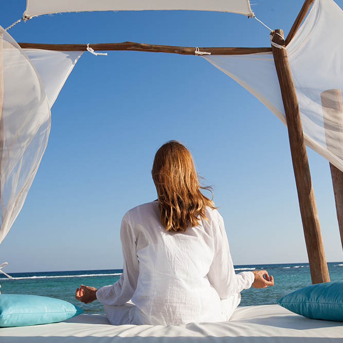 Woman in yoga pose sitting at the seashore under a shade