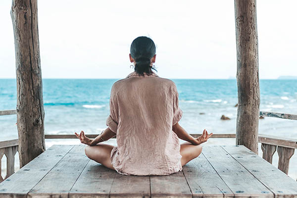 young woman meditating in a yoga pose in a gazebo at the beach