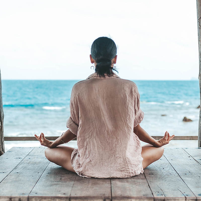 young woman meditating in a yoga pose in a gazebo at the beach