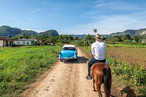 Classic car passes a man on horse in Vinales, Cuba