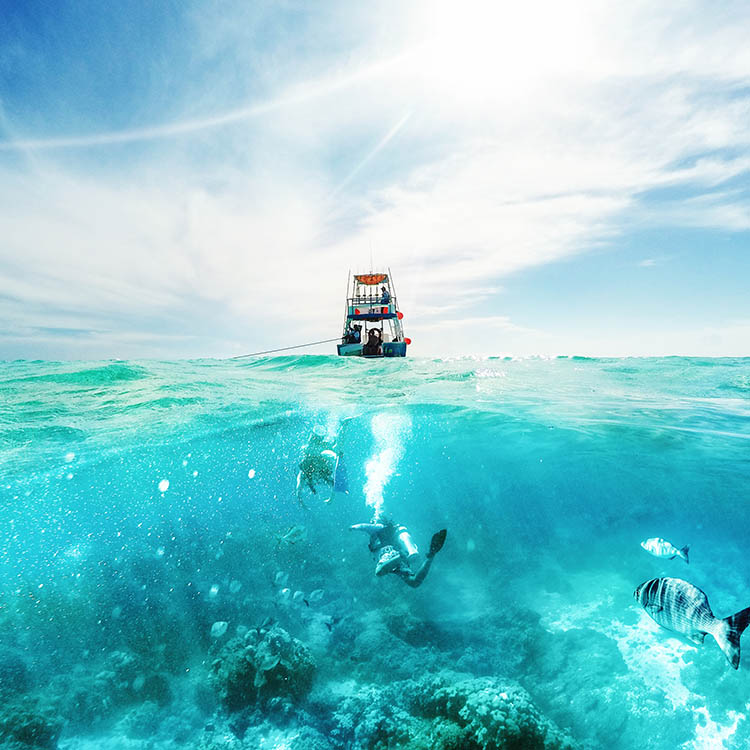 Scuba divers underwater and fishing boat above on the Caribbean Sea