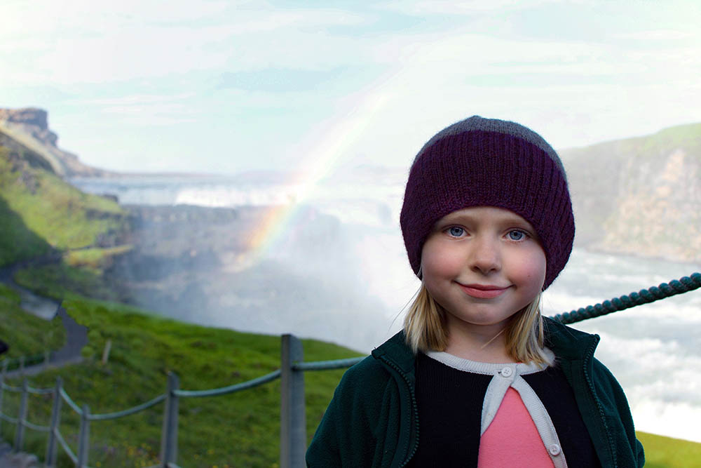 Young girl smiling with rainbow at Gullfoss Falls, Iceland