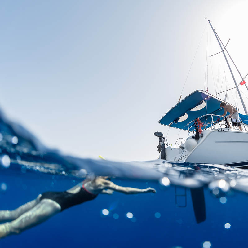 Split shot of woman swimming in a clear sea near sail boat