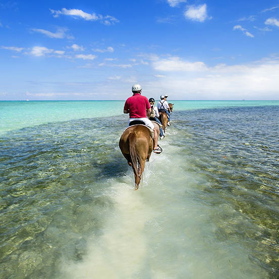 People riding on horse back on a Caribbean beach