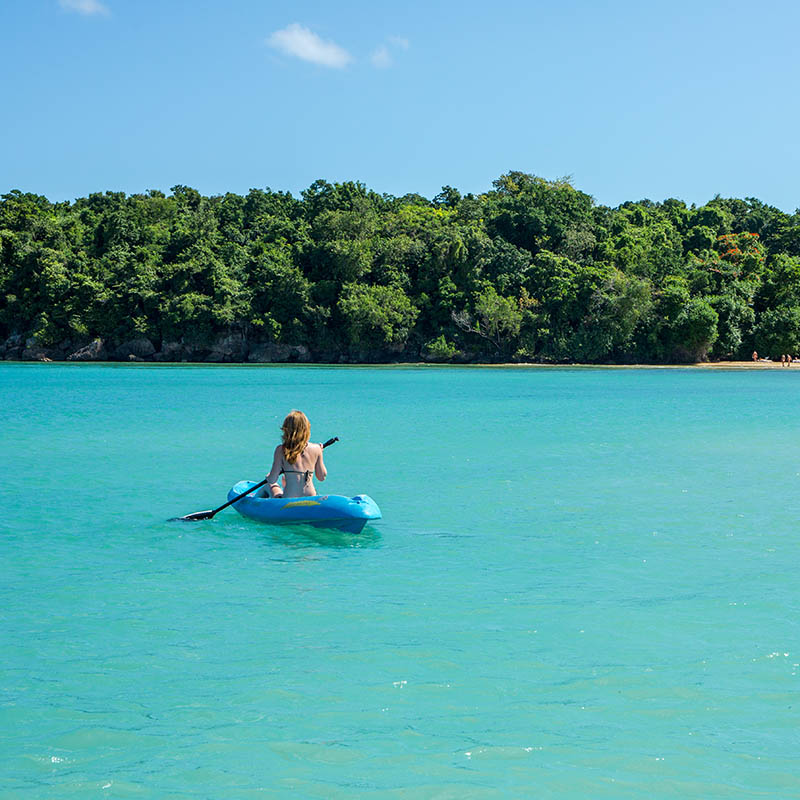 A young woman is paddling in a kayak on a turquoise ocean