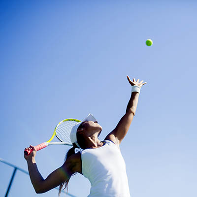 Female tennis player serving outdoors against a blue sky