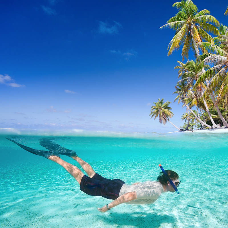 Man swimming in a clear tropical waters in front of exotic island