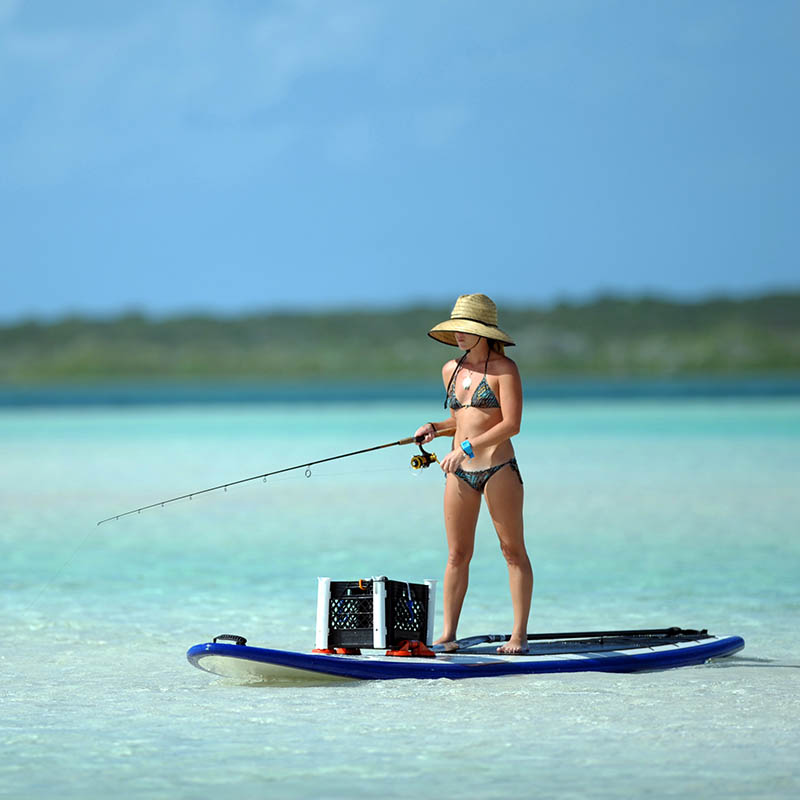 Woman in bikini fishing and paddle boarding