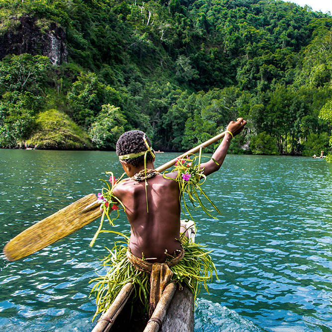 Young boy in traditional dress paddling a boat in Papua New Guinea