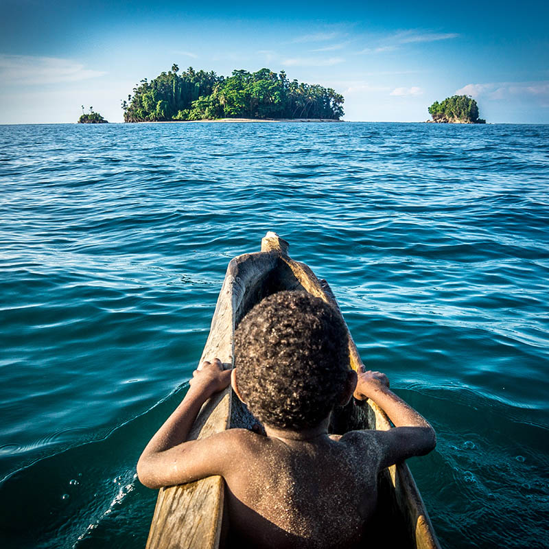 young boy in boat heading towards an island in papua new guinea