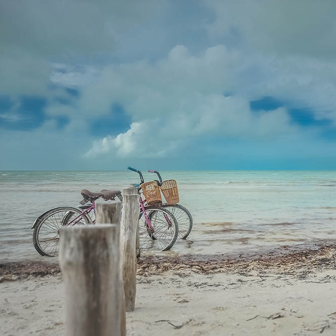 Two bicycles parked on a sandy beach with turquoise water