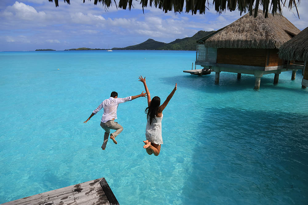 couple jumping into a lagoon in French Polynesia