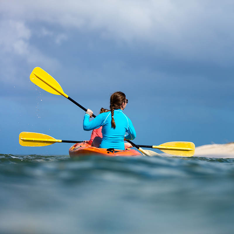 Family of mother and daughter paddling on kayaks at tropical ocean water during summer vacation