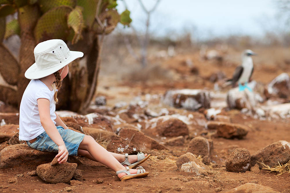 Young child sitting close to a blue footed booby on North Seymour Island, Galapagos