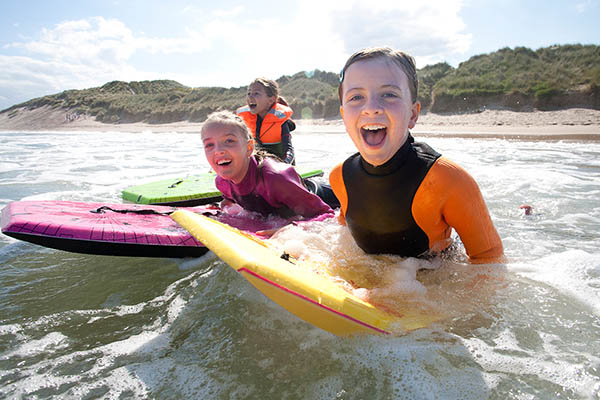 Three girls are smiling for the camera as they bodyboard in the sea together