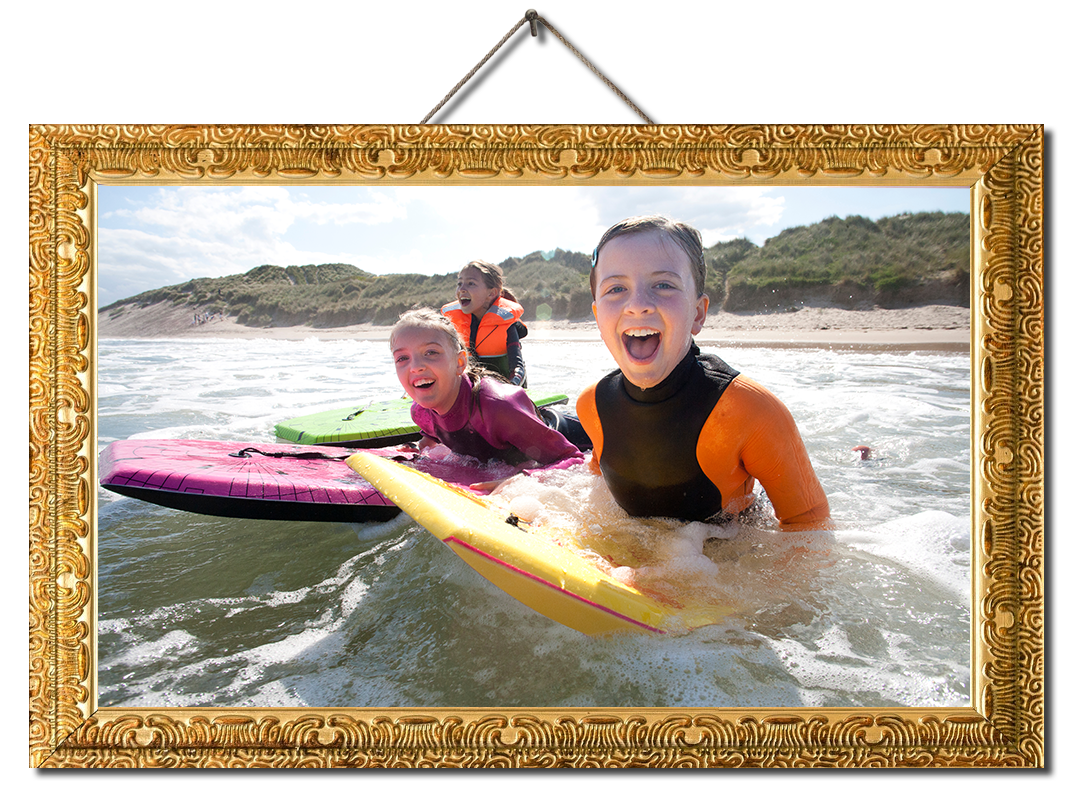 Three girls are smiling for the camera as they bodyboard in the sea together