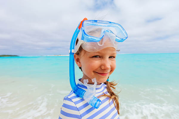 Adorable little girl with snorkeling equipment at beach during summer vacation