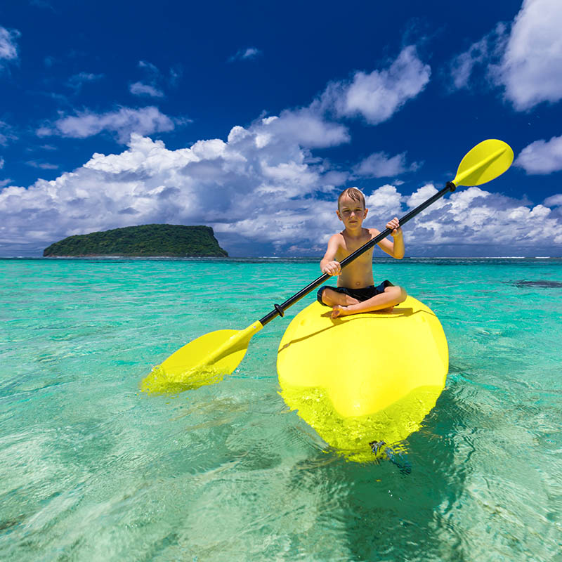 Young boy kayaking in front of an island in Samoa